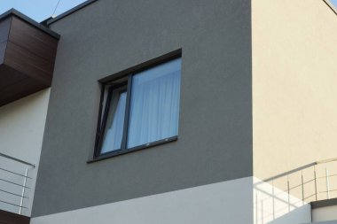 Binanın gri beton duvarında büyük siyah bir pencere var.