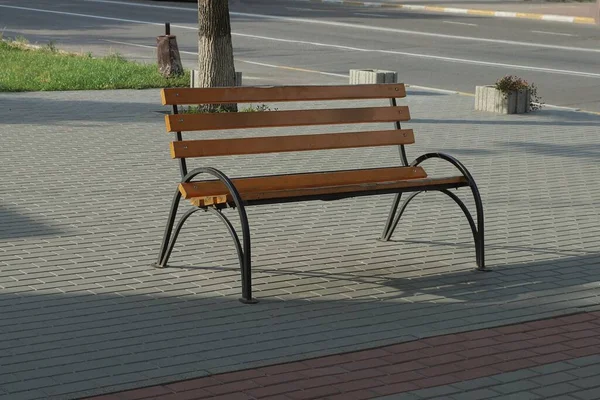 木製の板と黒い鉄で作られた茶色の空のベンチが通りの灰色の歩道に立っています — ストック写真