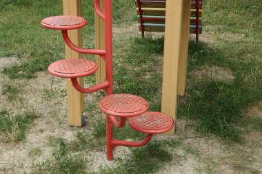 Kırmızı demir, metal bir merdivene basar. Yerde bir oyun parkında ve dışarıda yeşil çimenler.