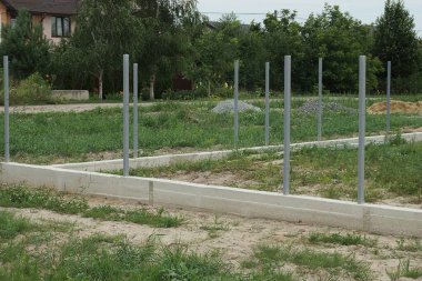 Yeşil çimenlikteki inşaat alanında demir sütunları olan gri beton bir temel.