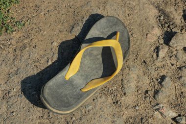 Kumsaldaki kumların üzerinde sarı bir koşum takımı olan eski, kirli, gri bir terlik.