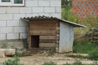Kahverengi boş bir ahşap köpek kulübesi dışarıda beyaz bir tuğla duvara karşı duruyor.