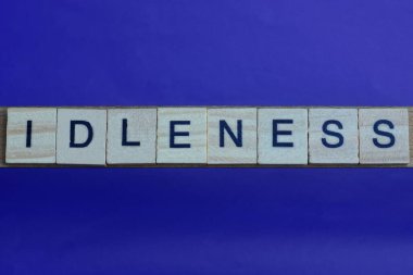 Gri kelime aylaklık üzerine metin küçük ahşap harflerle, eflatun arkaplanda siyah yazı tipi ile.