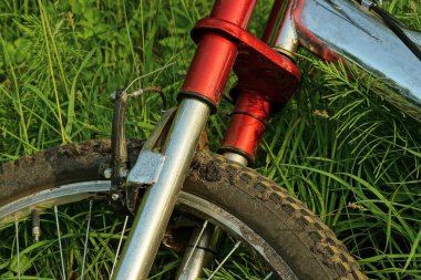 Demir çerçeveli bir bisikletin parçası ve dışarıdaki yeşil çimlerin üzerinde duran siyah lastikli bir tekerlek.