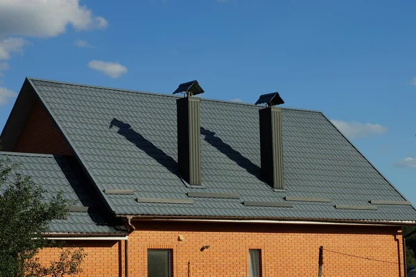 緑の瓦屋根の下のプライベート ブラウンのレンガ造りの家と青い空に対する2つの金属製の煙突 — ストック写真