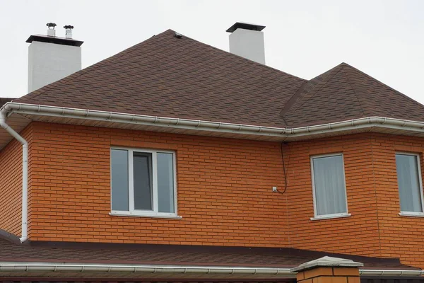 白い窓と茶色の瓦屋根の赤いレンガ造りの家灰色の空に対して煙突と — ストック写真