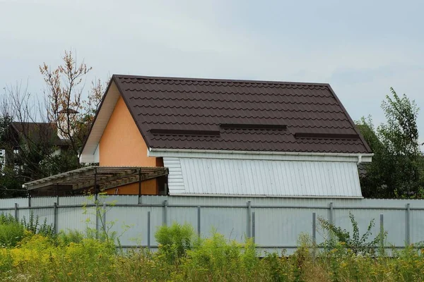 灰色の金属製の柵の後ろに茶色のタイル張りの屋根のある民家です — ストック写真