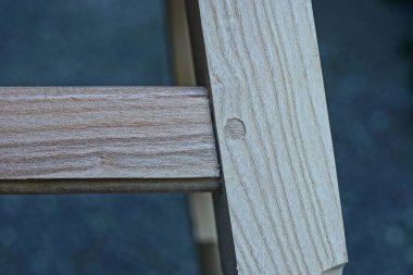 Gri arka planda kahverengi ahşap tahtalardan yapılmış bir sandalyenin parçası.