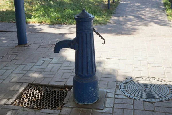 One old blue iron crane pump stands on a gray sidewalk in the street — Stock Image One Old Blue Iron Crane Pump Stands Gray Sidewalk Street Stock Image