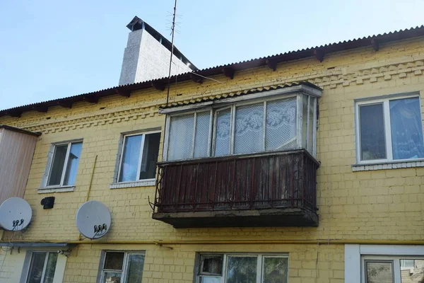 蓝色天空下有窗户的房子的黄色砖墙上的一个旧的封闭的棕色木制阳台 — 图库照片