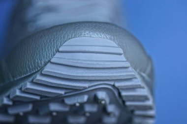 Mavi arka planda plastik tabanlı gri deri bir spor ayakkabının parçası.