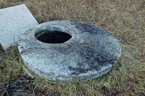 Kahverengi Çimlerin Üzerinde Açık Kapaklı Gri Yuvarlak Beton Lağım — Stok fotoğraf