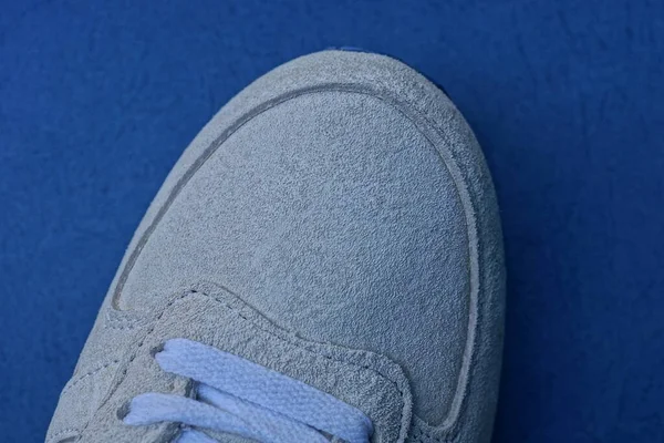 Beyaz dantelli gri süet bir spor ayakkabı mavi bir masada duruyor.