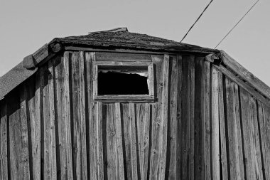 Gri gökyüzüne bakan küçük boş pencereli eski siyah ahşap çatı katı.