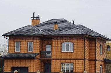 Gri gökyüzüne karşı kiremitli çatı pencereleri olan büyük kahverengi tuğla ev