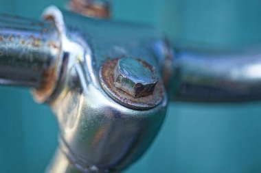 Eski bir demir cıvata yeşil arka plandaki eski bir bisiklet gidonuna vidalanmış.