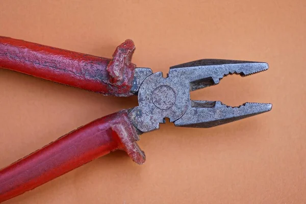 one old pliers tool with a red handle lies on a brown table