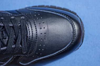 Büyük siyah deri bir ayakkabının parçası mavi bir masanın üzerinde.