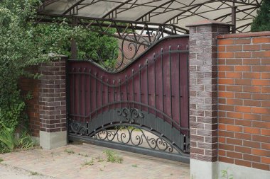 Siyah demir desenli bir metal kapı ve sokaktaki kahverengi tuğlalardan yapılmış bir çitin parçası.