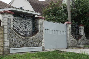 Büyük gri bir demir kapı ve kırsal bir sokakta çitin bir parçası.