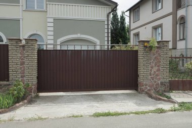 Büyük kahverengi demir kapı ve dışarıdaki gri taş ve tuğlalardan yapılmış bir çitin parçası.