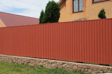Sokakta yeşil çimlerde, taş bir temele kurulmuş uzun metal bir çit.