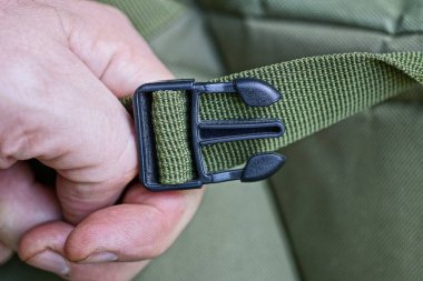 Sırt çantasının yeşil kayışında siyah plastik bir karabina var.