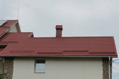 Gri gökyüzüne karşı kırmızı kiremitli çatının altında kahverengi bir duvarda penceresi olan özel bir evin tavan arası.