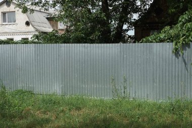 Kırsal bir sokakta yeşil çimlerde gri metal bir çitin bir parçası.