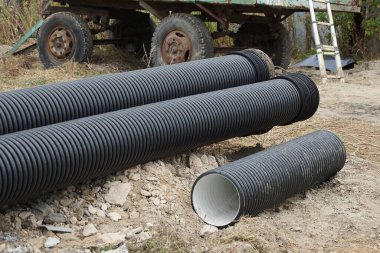 Dışarıda gri zeminde üç büyük siyah plastik lağım borusu var.