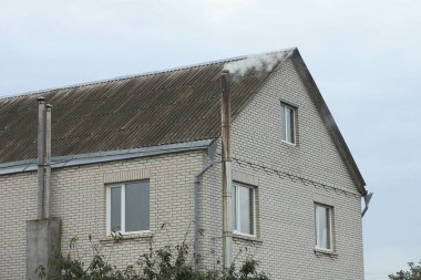 Gri bir çatı altında pencereleri olan büyük beyaz tuğla bir ev.