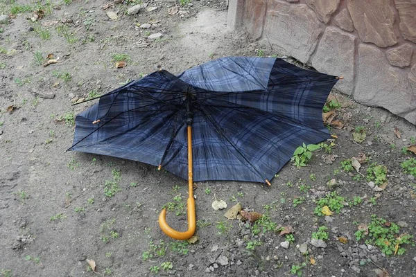 one blue broken umbrella with brown wooden handle lies on gray ground outside