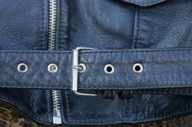 Gri metal tokalı ve fermuarlı siyah deri bir ceketin parçası.