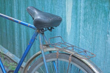 Mavi çerçeveli ve bagaj rafı olan eski bir bisikletin parçası ve yazlık bir sokakta yeşil bir duvara karşı siyah deri bir koltuk.