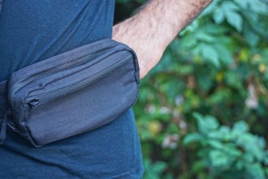 Gri, küçük, kumaş bir el çantası bir yaz caddesinde erkek kemerine asılı.