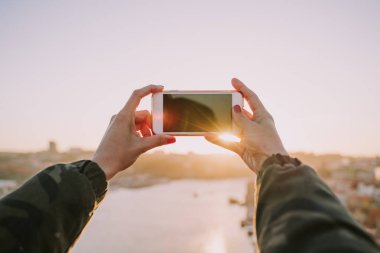 Yakından kapatın. Gün batımında fotoğraf çekerken cep telefonu tutan bir kadının elleri
