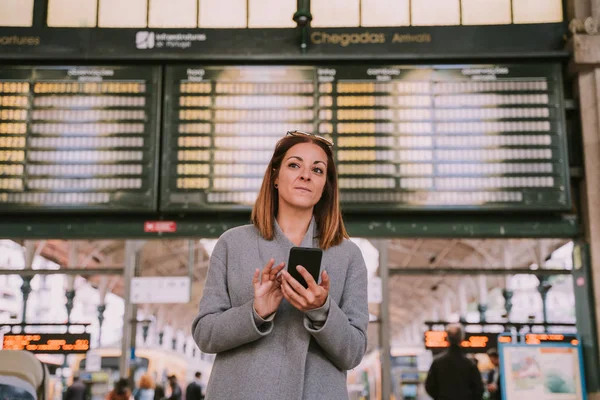 Mujer joven y hermosa esperando en la estación con su teléfono en sus manos — Foto de Stock