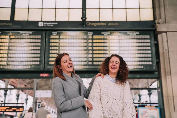Dwie piękne kobiety śmieją się razem na dworcu kolejowym — Zdjęcie stockowe