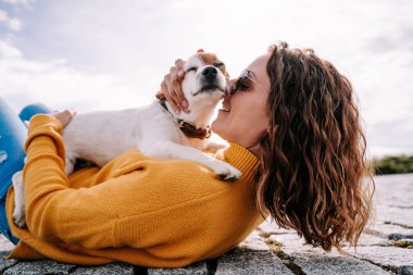 Parkta uzanmış küçük sevimli köpeğine sarılan güzel bir kadın. Madrid 'de güneşli bir günün tadını çıkarıyorlar. Aile köpeği açık hava yaşam tarzı
