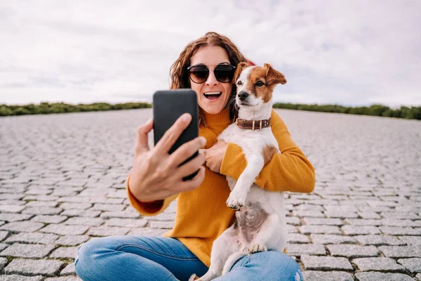 かわいい犬と公園に座っている美しい女性 彼女は電話で犬と自画像写真を撮っている ペットとテクノロジーライフスタイル — ストック写真