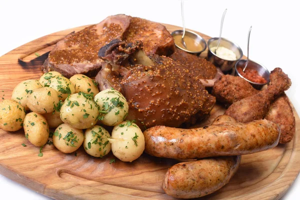 Meat snacks plate. red, white and yellow sauces on a wood. Sausage assortment with Fried pork knuckle, fried chicken and young potatoes on white background. Close up of beer snacks set