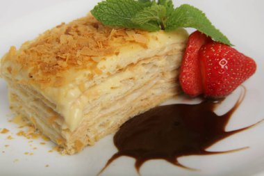 Kek Napolyon çilek, nane ve çikolata sosu ile süslenmiş bir parça. beyaz plaka üzerinde ışık arka plan üzerinde izole