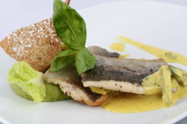 Biberiye soslu sebzeli beyaz balık parçaları ve beyaz arka planda ince bir dilim kızarmış ekmek. Masa çok güzel. Restoran yemeği.