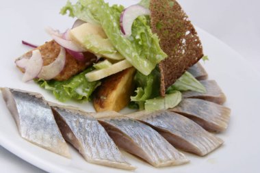 Beyaz arka plan üzerinde patates dilimleri, yeşillik, kırmızı soğan ve çavdar ekmeği ile ringa balığı balık. 