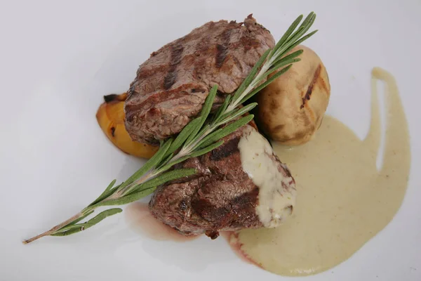Appetizer steak of medium rarity with rosemary leaves and sauce.