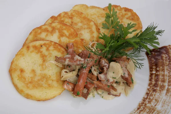 potato pancakes with mushroom sauce and fried mushrooms (chanterelles). Close-up on a white plate