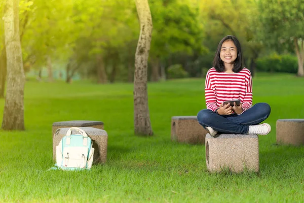 在阳光明媚的夏日 在学校公园使用数码平板电脑的亚洲学生女孩 — 图库照片