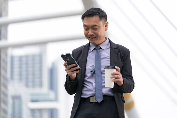 Asiatischer Geschäftsmann steht und hält Handy mit Geschäftsleuten Stockfoto