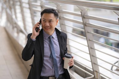 Asyalı İşadamı yürüyüş ve busin ile cep telefonu konuşuyor