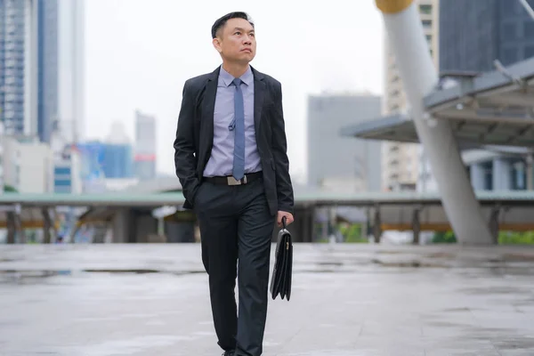 Asian Businessman walking and holding briefcase with business of